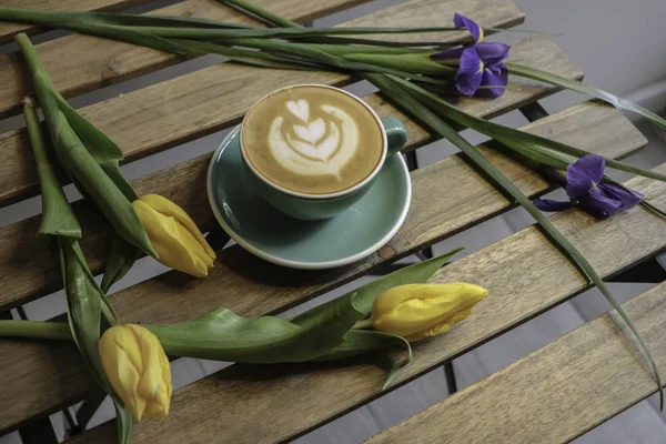 Kız bir fincan kahve tutar. Kapuçino. Latte. Çiçekler, Lale ahşap bir masa kahve. 8 Mart.