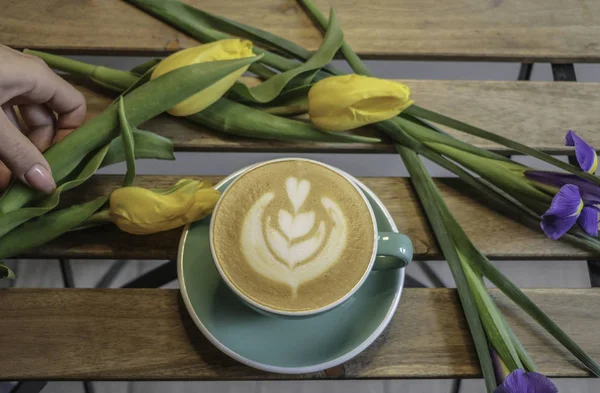 Kız bir fincan kahve tutar. Kapuçino. Latte. Çiçekler, Lale ahşap bir masa kahve. 8 Mart.