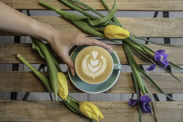 Kız bir fincan kahve tutar. Kapuçino. Latte. Çiçekler, Lale ahşap bir masa kahve. 8 Mart.