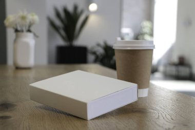 Masada bir kahve bardağı ve beyaz bir kitap bir mockup olduğunu. Kahve evi. Cafe arka plan. Çiçekler beyaz Notepad.