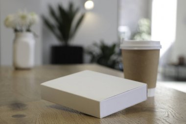 Masada bir kahve bardağı ve beyaz bir kitap bir mockup olduğunu. Kahve evi. Cafe arka plan. Çiçekler beyaz Notepad.