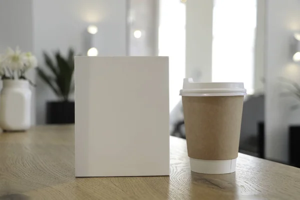 Masada bir kahve bardağı ve beyaz bir kitap bir mockup olduğunu. Kahve evi. Cafe arka plan. Çiçekler beyaz Notepad.