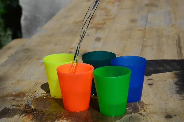 Su dolu ahşap bir masa üzerinde renkli plastik bardaklar