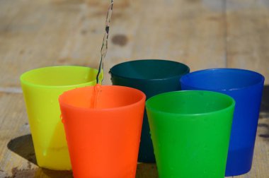 Su dolu ahşap bir masa üzerinde renkli plastik bardaklar