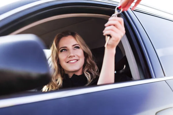 Μια ελκυστική γυναίκα σε ένα αυτοκίνητο παίρνει τα κλειδιά του αυτοκινήτου. Ενοικίαση ή αγορά του auto. — Φωτογραφία Αρχείου