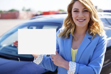Beyaz boş poster tutarak araba ile duran kadın.