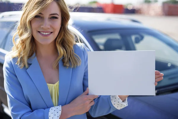 Žena stojící auto drží bílé prázdné plakát. — Stock fotografie