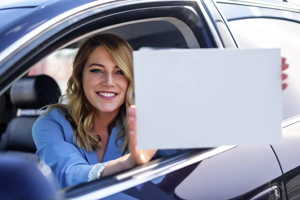 Mujer sentada en el coche y sosteniendo un cartel blanco en blanco . —  Fotos de Stock