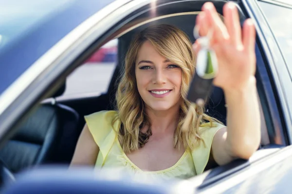 Uma mulher atraente em um carro tem uma chave de carro em sua mão . — Fotografia de Stock
