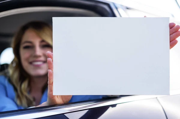 Woman sitting in the car and holding a white blank poster. — Stock Photo, Image