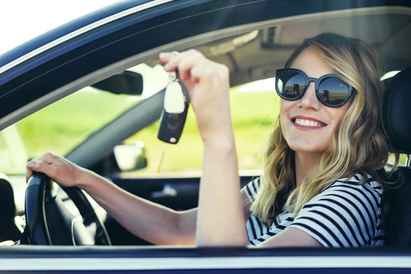 Una mujer atractiva en un coche tiene una llave en la mano . — Foto de Stock