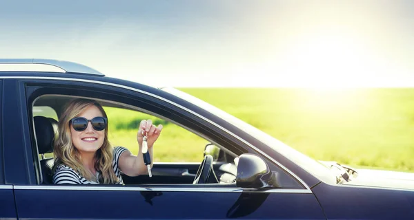 En attraktiv kvinna i en bil håller en bilnyckel i sin hand. Hyra eller köp av auto - konceptet. — Stockfoto