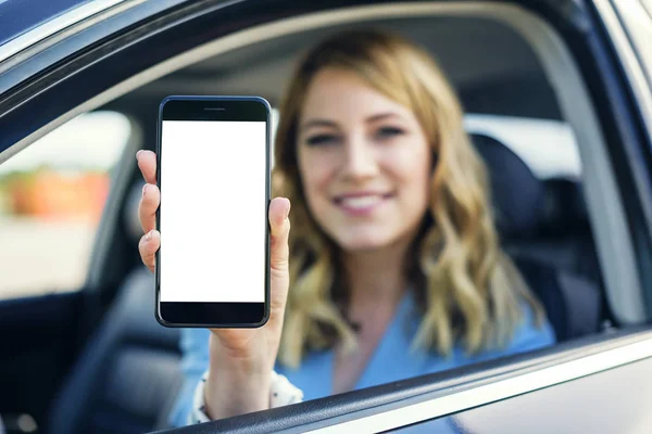 Mujer joven en auto muestra teléfono inteligente con pantalla en blanco . — Foto de Stock