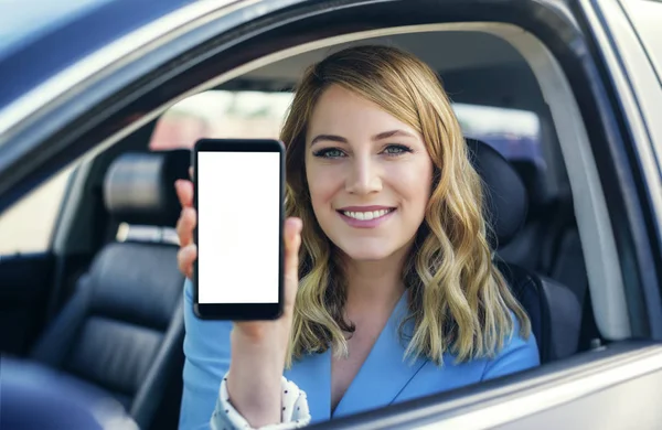 Mujer joven en auto muestra teléfono inteligente con pantalla en blanco . —  Fotos de Stock