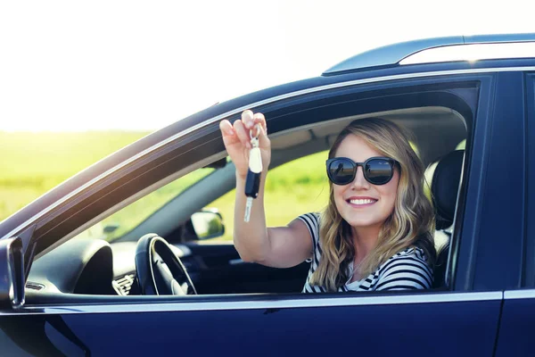 Una mujer atractiva en un coche tiene una llave en la mano. Alquiler o compra de auto - concepto . — Foto de Stock