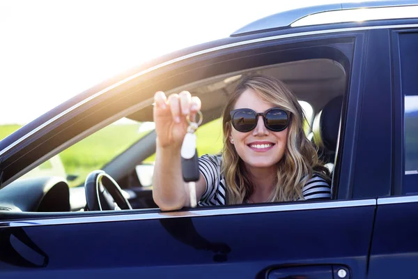 An attractive woman in a car holds a car key in her hand. Rent or purchase of auto - concept.