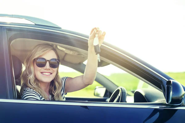 Una mujer atractiva en un coche tiene una llave en la mano. Alquiler o compra de auto - concepto . — Foto de Stock