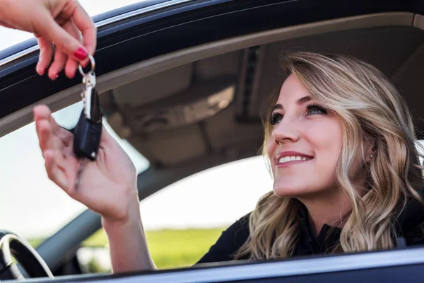 Uma mulher atraente num carro recebe as chaves do carro. Aluguer ou compra de automóveis . — Fotografia de Stock