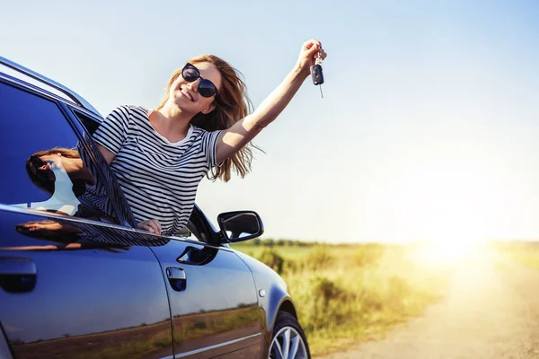 Een aantrekkelijke vrouw in een auto houdt een auto sleutel in haar hand. — Stockfoto