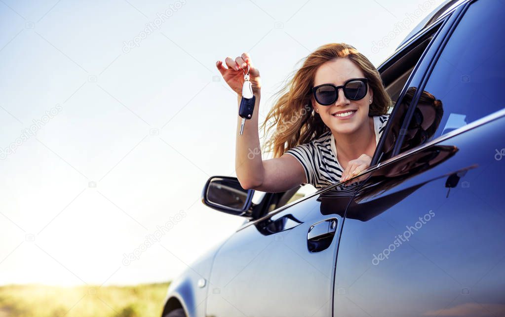 An attractive woman in a car holds a car key in her hand.