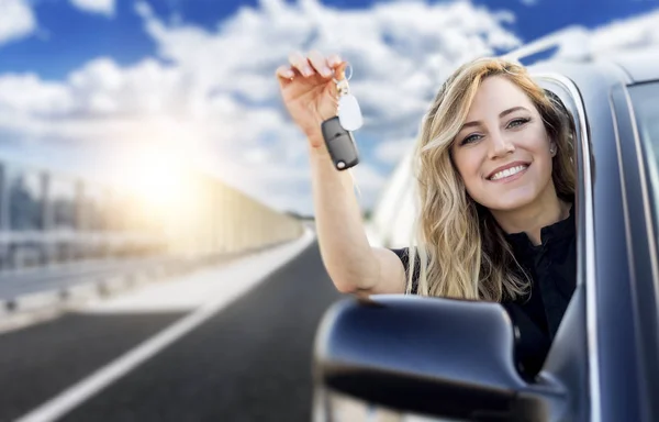 Uma mulher atraente em um carro tem uma chave de carro em sua mão . — Fotografia de Stock