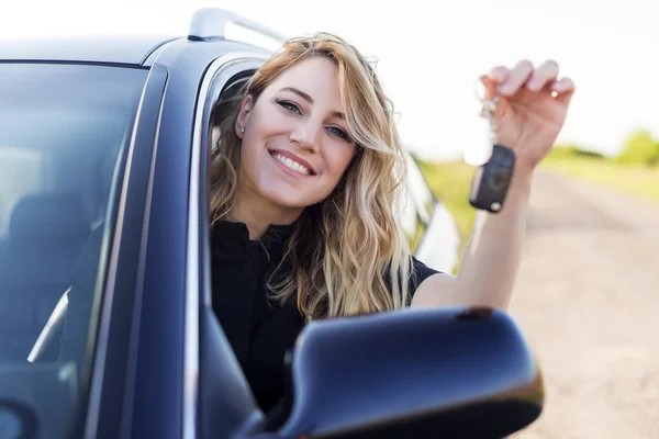 Uma mulher atraente em um carro tem uma chave de carro em sua mão . — Fotografia de Stock