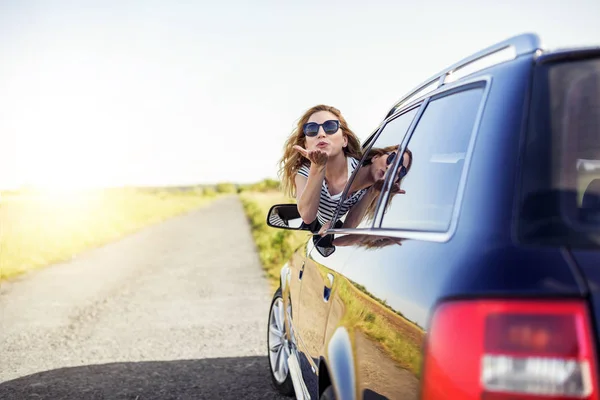 Attraktivt leende kvinna skickar en air kyss från bilfönstret på en sommardag. — Stockfoto