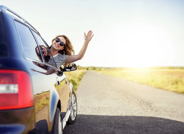 Belle femme souriante agitant la main de la fenêtre de la voiture un jour d'été . — Photo