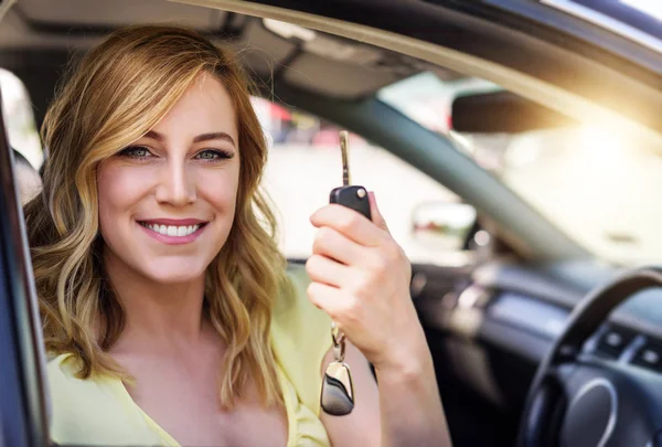 An attractive woman in a car holds a car key in her hand. Rent or purchase of auto - concept.