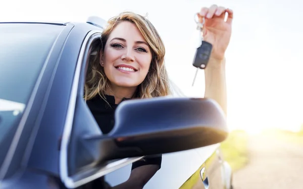 Una mujer atractiva en un coche tiene una llave en la mano . — Foto de Stock