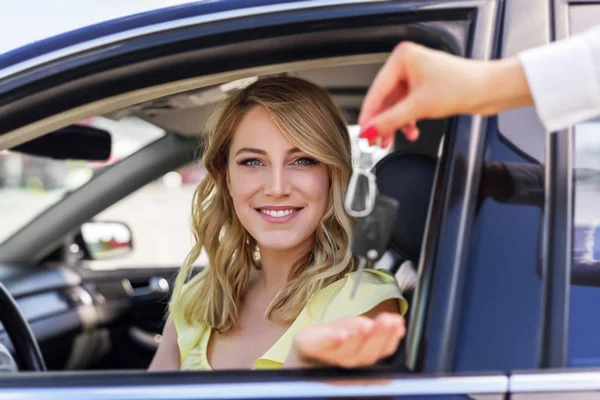 Una mujer atractiva en un coche consigue las llaves del coche. Alquiler o compra de auto . —  Fotos de Stock