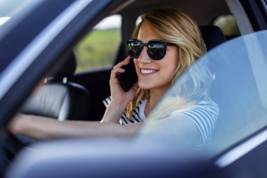 Kadın arabada telefonda konuşuyor.