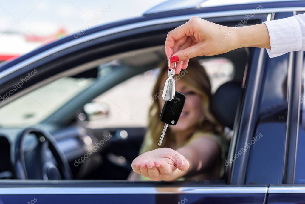 An attractive woman in a car gets the car keys. Rent or purchase of auto.