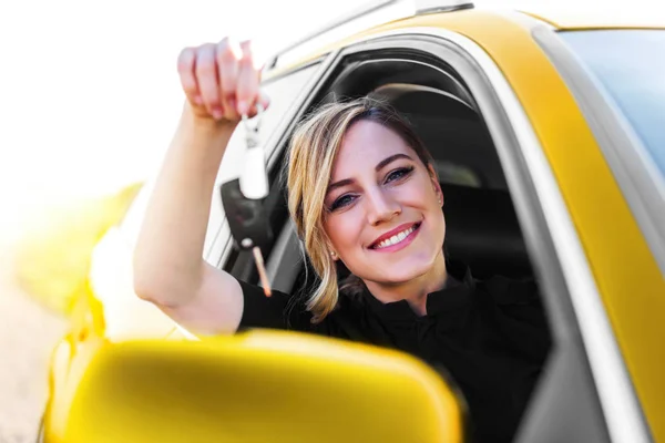 Een aantrekkelijke vrouw in de gele auto houdt een auto sleutel in haar hand. — Stockfoto