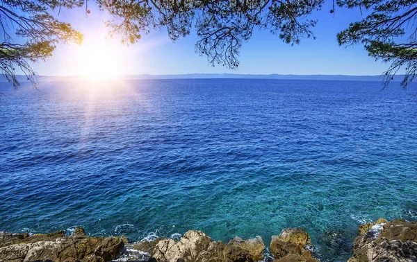 A costa pedregosa do mar azul e o sol no horizonte — Fotografia de Stock