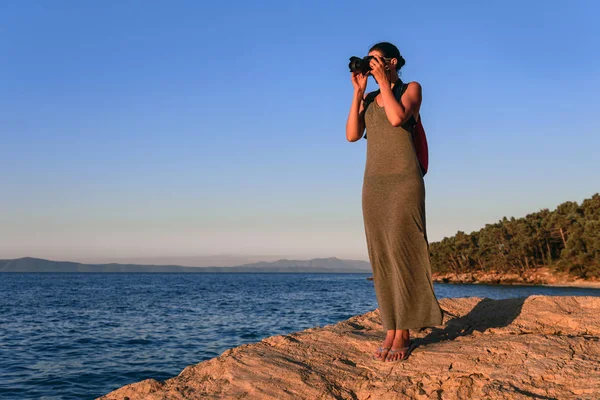 Woman with a camera photographing the sunset on the sea coast. — Stock Photo, Image