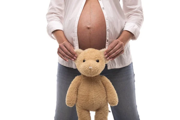 Zwanger meisje een teddybeer te houden door de oren op witte achtergrond. — Stockfoto