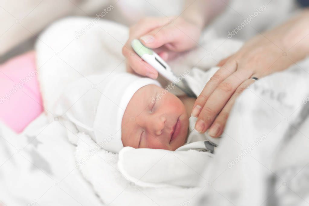 Baby in the crib measures body temperature. Mom measures the babys body temperature with a thermometer.