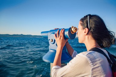 Young woman looks in a telescope or binoculars by the sea.