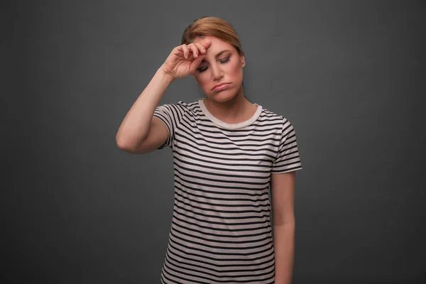 Tired woman on gray background. The blonde holds her head with her eyes closed. — Stock Photo, Image