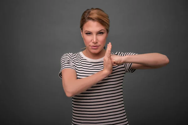 Beautiful woman shows a lock sign, resting her fist in the palm on gray background. — Stock Photo, Image