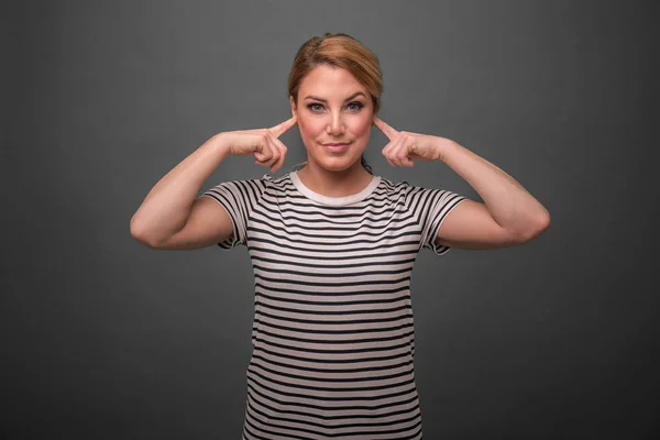 Attractive woman covers her ears with fingers on a gray background. — Stock Photo, Image
