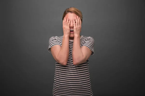 Ung kvinna döljer ansiktet på en grå bakgrund. — Stockfoto