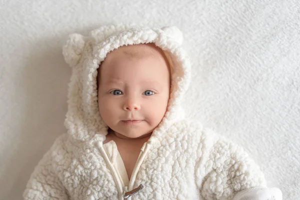 Beautiful baby girl in a warm white suit lying on a bed. — Stock Photo, Image