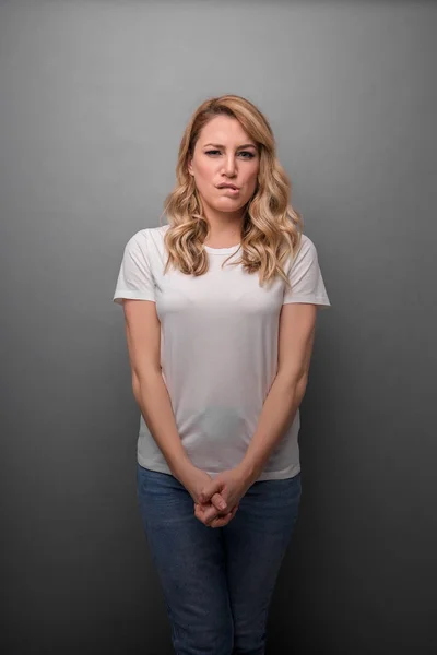 Una giovane donna sta strizzando gli occhi a una smorfia acida mentre sta in piedi su uno sfondo grigio . — Foto Stock
