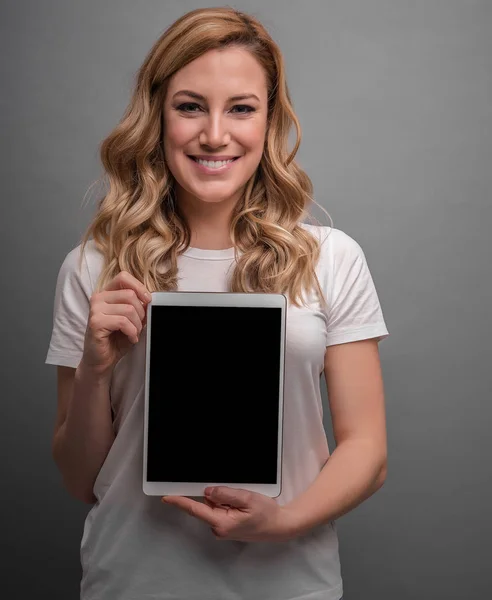 Attractive blonde is holding tablet pc on a gray background. — Stock Photo, Image