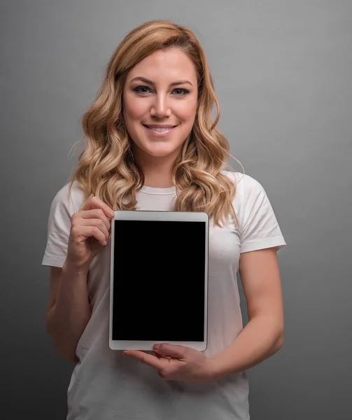 Attraktive Blondine hält Tablet-PC auf grauem Hintergrund. — Stockfoto