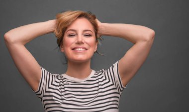 Genç kadın elle gri arka plan üzerinde başının arkasında rahatlatıcı.