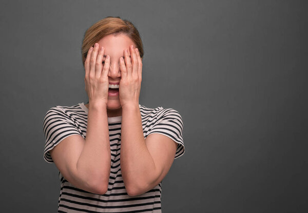 Молодая женщина прячет лицо на сером фоне
.