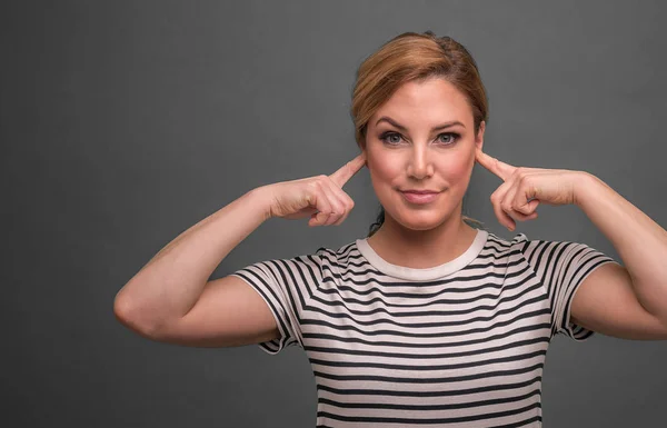 Attractive woman covers her ears with fingers on a gray background. — Stock Photo, Image